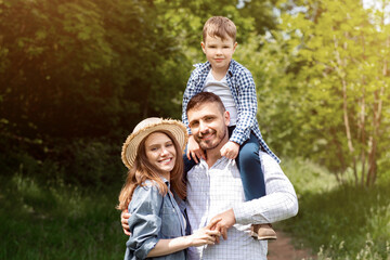 Fototapeta premium Portrait of loving parents with their little son standing together in forest on bright sunny day