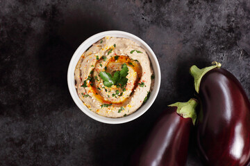 Bowl with baba ganoush, eggplant hummus on black background, from above overhead top view,...