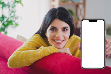 Cheerful young woman indoors showing smartphone screen in cozy living room