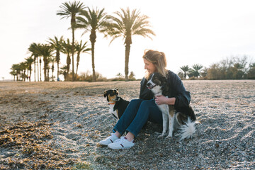 Woman sitting on beach with two dogs enjoying golden hour light