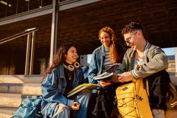 Fototapeta premium Cheerful university or college students sharing notes and studying together outdoors