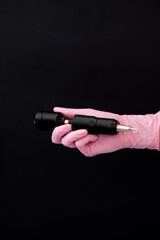 Permanent makeup. Hands of a girl in pink gloves holding a permanent machine on a black background
