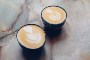 Two cups of fresh delicious cappuccino coffee with beautiful latte art on marble background.  Morning scene with hot drink.