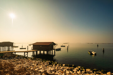 winter sunset over the Scardovari lagoon with fishing boats and cabins inside the delta of the...