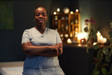 African American woman wearing uniform, standing with arms crossed in a spa, smiling warmly