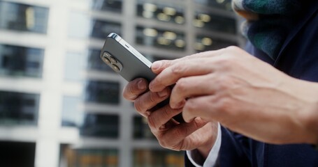 A man is typing on his mobile phone while standing outdoors near an office building. Close-up of male hands with smartphone, unrecognizable person. Video in 4k, red komodo