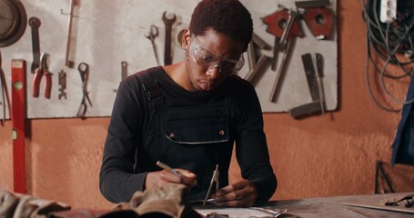 Work on creating a sketch of a future product in a blacksmith's workshop. An African-American man...