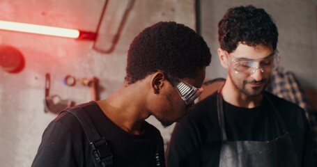 Two blacksmiths of different nationalities in work clothes are considering a sketch of a future product, working together and using a tablet, close-up. 4k video, red komodo