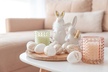 Easter eggs, candles and white ceramic rabbits on wooden table in interior of living room
