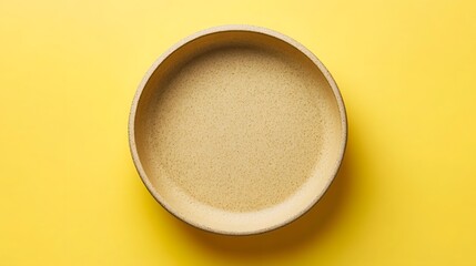 A simple, smooth, beige bowl centered on a vibrant yellow background, showcasing minimalism
