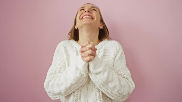 Young woman celebrating success, blonde winner wearing sweater excited and mad with arms raised on isolated pink background
