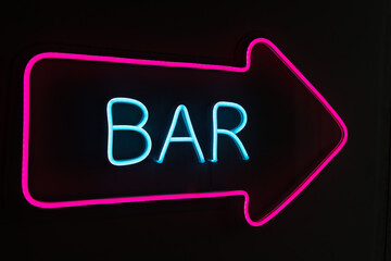 Neon sign for a bar with the inscription BAR and a pointer arrow.A bright light pointer pointing in the direction of the bar at night on the street.
