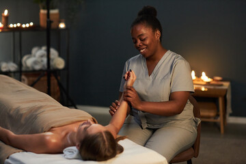 Masseuse smiling warmly, providing relaxing massage therapy in serene, candlelit room, enhancing...