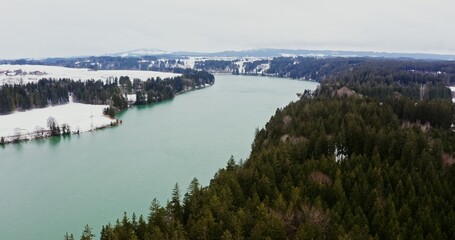 Fototapeta premium Video filming from a bird's eye view, from a drone . View of a wide river flowing through forests and snowy fields. Village on the banks of the river, drone video