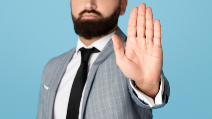 Cropped view of millennial businessman refusing something, showing STOP gesture on blue studio...
