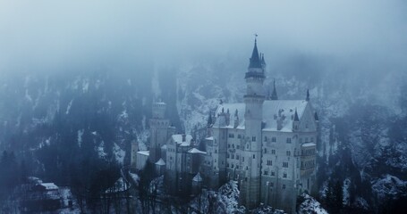 Obraz premium Overview of Hohenzollern Castle from a dynamic motion quadcopter, bird's eye view close-up video footage on a winter day. Foggy haze over castle, located on top of a hill overgrown with spruce forest
