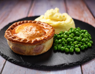 Traditional British pie served on a slate plate with potato mash and peas