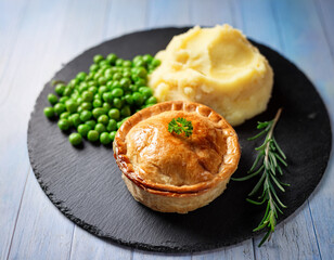 Traditional British pie served on a slate plate with potato mash and peas