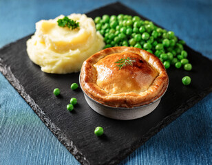 Traditional British pie served on a slate plate with potato mash and peas