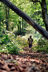 Young man walking along a path in a dense sunny forest in the mountains