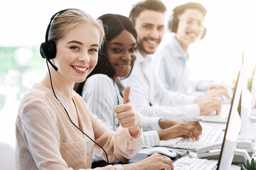 Multiethnic call centre consultants with headsets smiling at camera in modern office