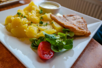Lunch at the restaurant. Potatoes with a piece of fried chicken fillet on a square plate. Tomato and greens close-up
