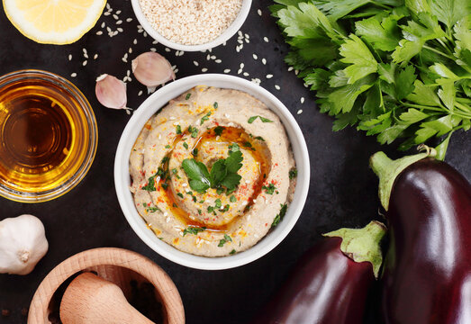 Bowl with baba ganoush, eggplant hummus on black background with ingredients, from above overhead top view, traditional Middle Eastern cuisine concept