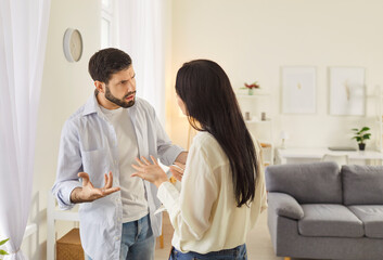 Obraz premium Young family couple arguing in living room, showing signs of disagreement. Angry husband and wife quarreling, expressing frustration and disappointment. Relationship problems and divorce concept.