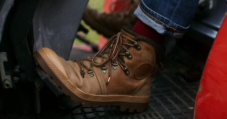 A man presses the pedal of an agricultural machine, close-up of male feet in stylish boots, the...