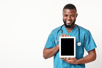 Smiling African American guy doctor demonstrating blank digital tablet screen over white...