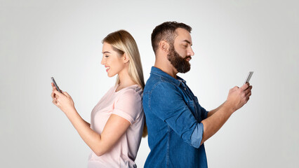 A married couple stands back to back, each engrossed in their smartphones. They appear disconnected...