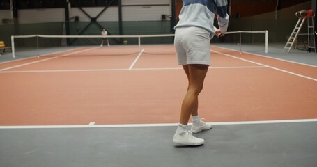 Obraz premium Rear view of an athletic young European woman jumping up and down while playing tennis. Strong legs in short blinkers close-up