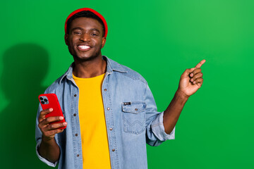 Happy young man in casual outfit holding a smartphone and pointing with a cheerful expression under...