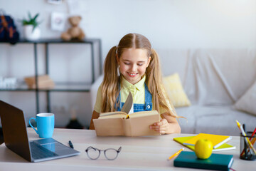 Doing Homework. Portrait of charming teenage girl reading paper book, sitting at desk, copy space