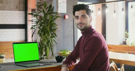 Young brunette man with stubble on his face smiling looking straight into the camera while sitting...