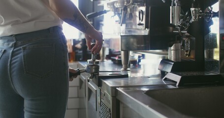 Young woman barista presses the ground coffee, preparing it for the coffee machine. The processes...