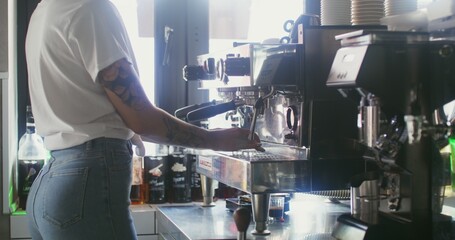 Young beautiful woman barista turns on the coffee machine, a thin stream of hot drink begins to flow into the glass. Details of professional coffee preparation