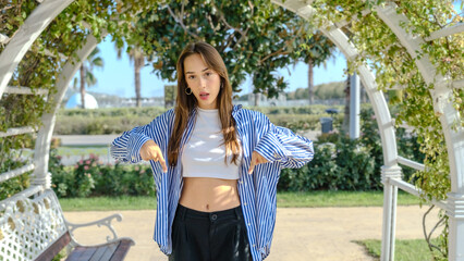 A young businesswoman in a tree-filled park on a spring day, looking at the camera while pointing to specific spots with her index finger