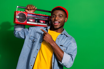 Happy stylish young man holding a red retro radio on his shoulder in front of a vibrant green background
