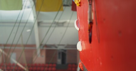 A young man, with a focused look, climbs up the climbing wall, attaching a safety rope to the hooks...