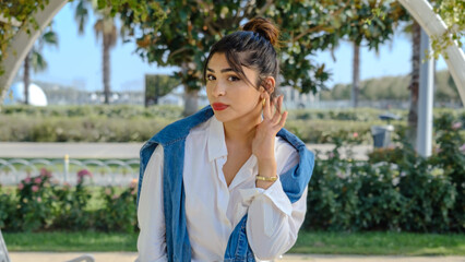 A young brunette businesswoman in a tree-filled park on a spring day, looking at the camera with a...