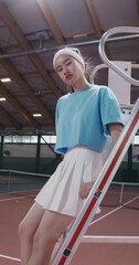 A woman tennis player of Asian appearance in a short skirt sits on the stairs of the referee's...