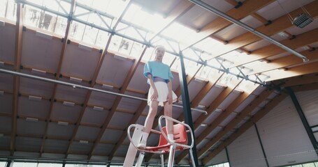 A young woman tennis player of Asian appearance, in a short skirt stands on a high referee's chair...