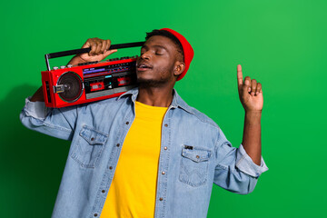 Stylish young man enjoying music with a retro boombox on a vibrant green background