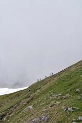People climb a mountain with stones through a gray cloud