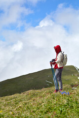 A female hiker stands on an alpine mountainside against a backdrop of cumulus clouds