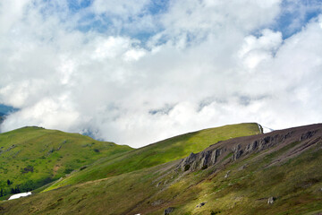 Cumulus clouds against green alpine meadows and mountains in the evening