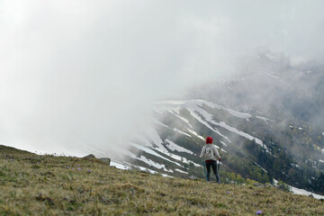 A man in the clouds stands on a mountain side and is inspired by the beautiful landscape