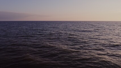 Sea distance with small ripples of waves, no shore, video from a drone. Sunset sky with pink reflections.