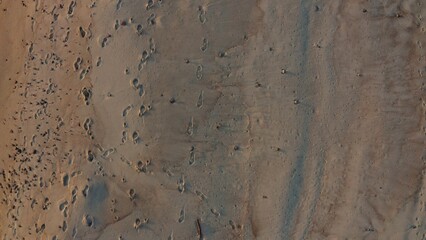 Top view, footprints on wet sand on the seashore washed by foamy waves. Video from the drone.